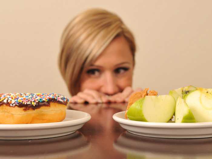 Выбор между пончиком и яблоком Женщина не может выбрать между пончиком и яблоками