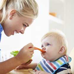 Малыш и мама за обедом Мама кормит малыша с ложки