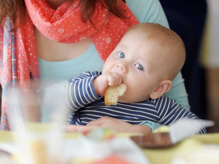 Малыш на руках у мамы Малыш жует хлеб на руках у мамы