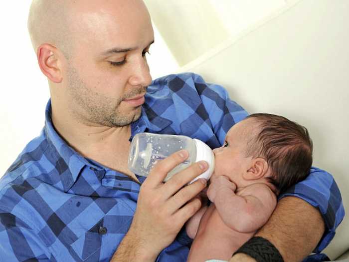 Папа кормит малыша Малыш ест из бутылки на руках у папы