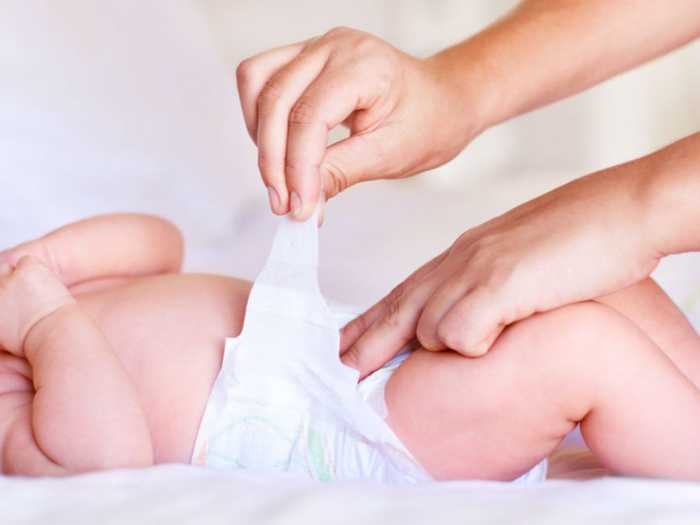 Малыш в памперсе Мама одевает ребенка в подгузник