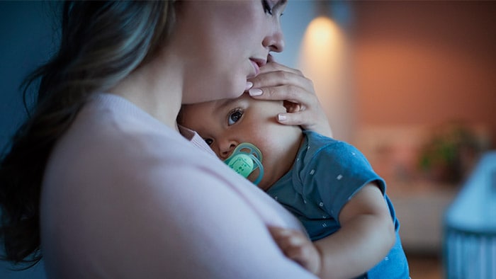 Малыш с пустышкой на руках у мамы. Пустышка помогает удовлетворить естественный сосательный рефлекс малыша.