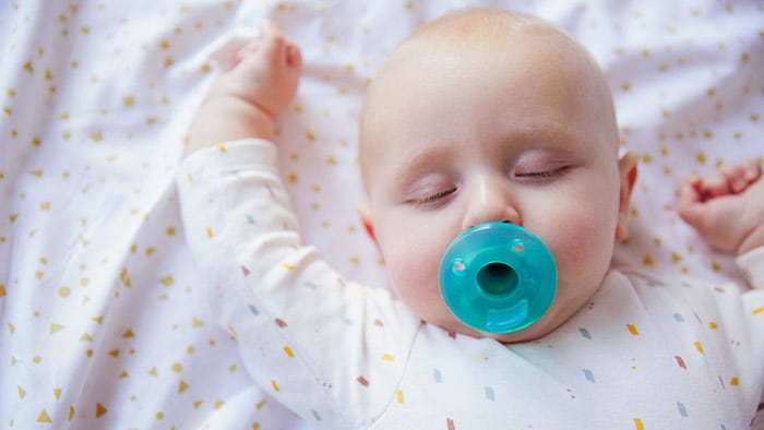 Новорожденный спит с пустышкой во рту. Использование пустышки помогает ребенку успокоиться и уснуть.